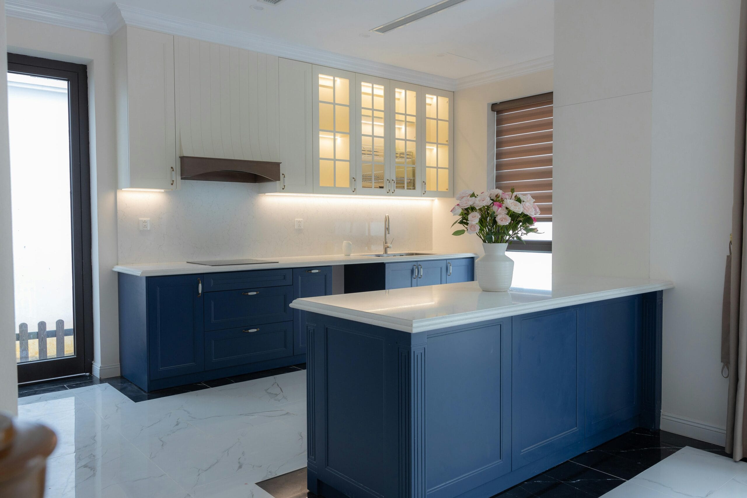 Elegant kitchen with blue cabinets, white countertops, and a vase of flowers.